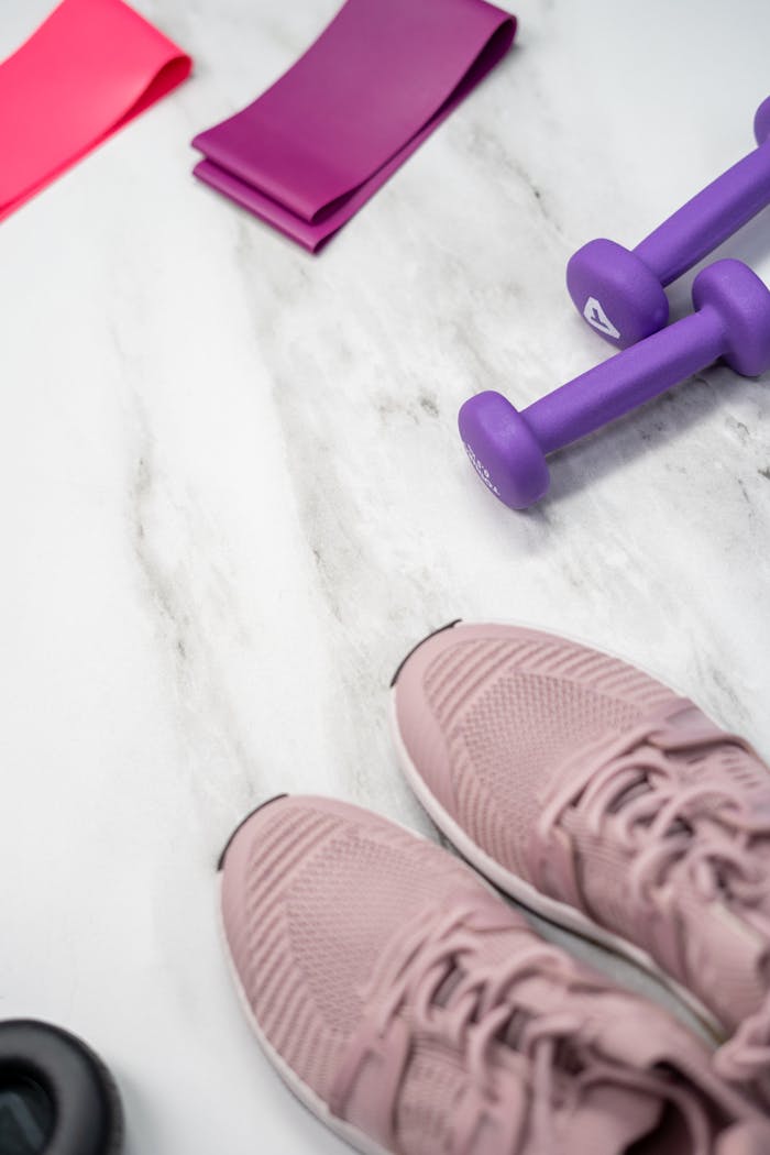 Home Flat lay of pastel pink fitness gear including sneakers and dumbbells on marble texture.