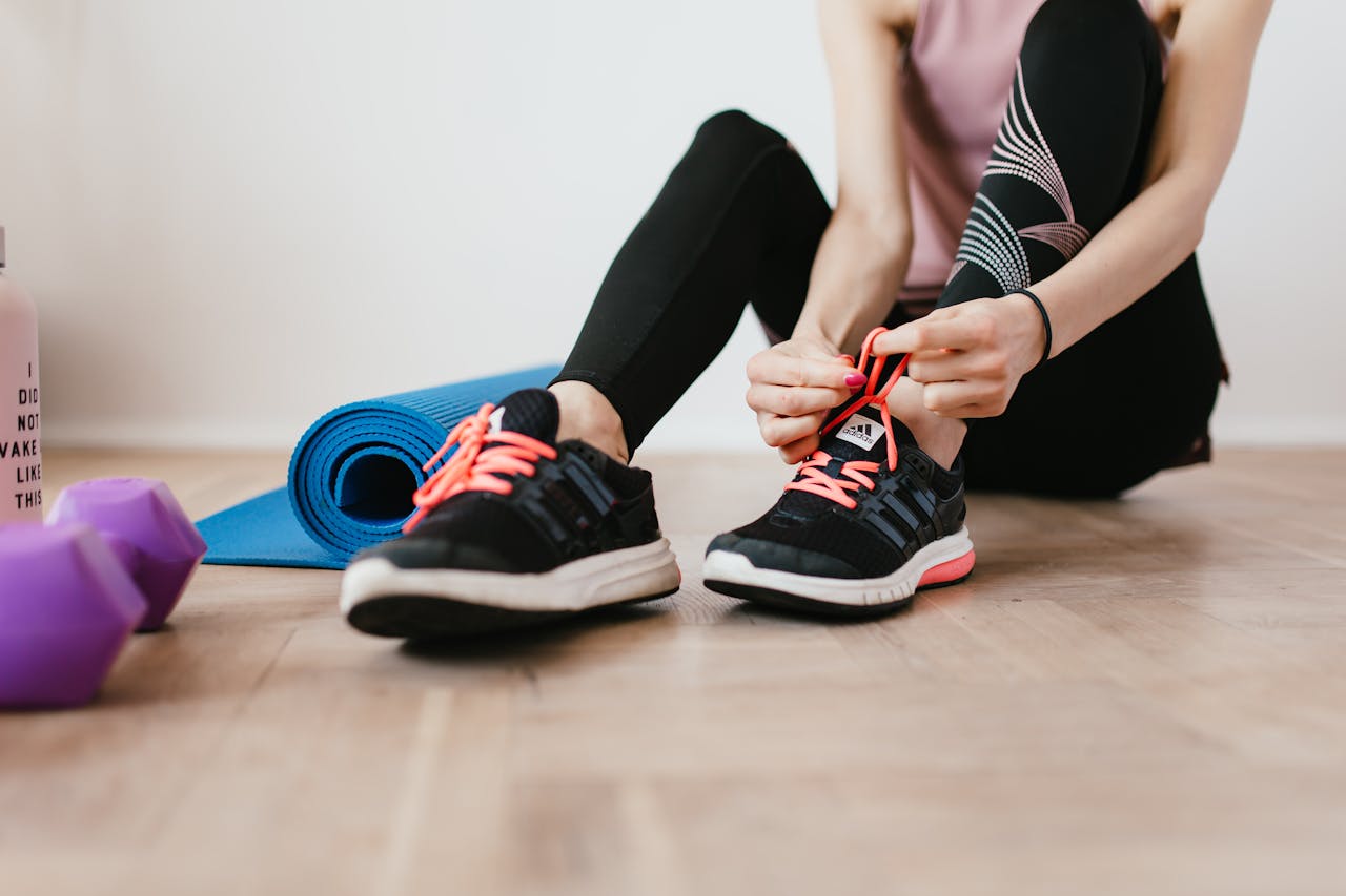 Home Fit woman tying shoelaces, preparing for indoor workout with yoga mat and dumbbells.